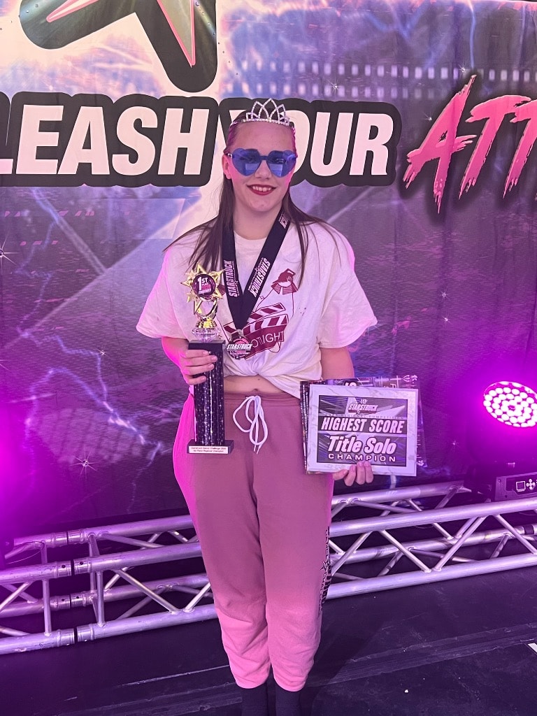 Dancer holding trophy and Title Solo Champion plaque at competition