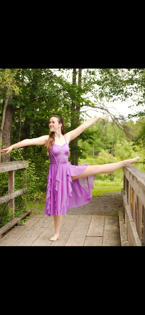 Dancer in purple dress performing arabesque on a bridge outdoors