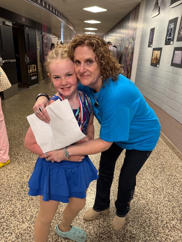 Miss Nicky hugging a young dancer holding an award backstage